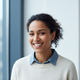 A diverse woman in her late 20s to early 30s, smiling genuinely with a warm, approachable expression.